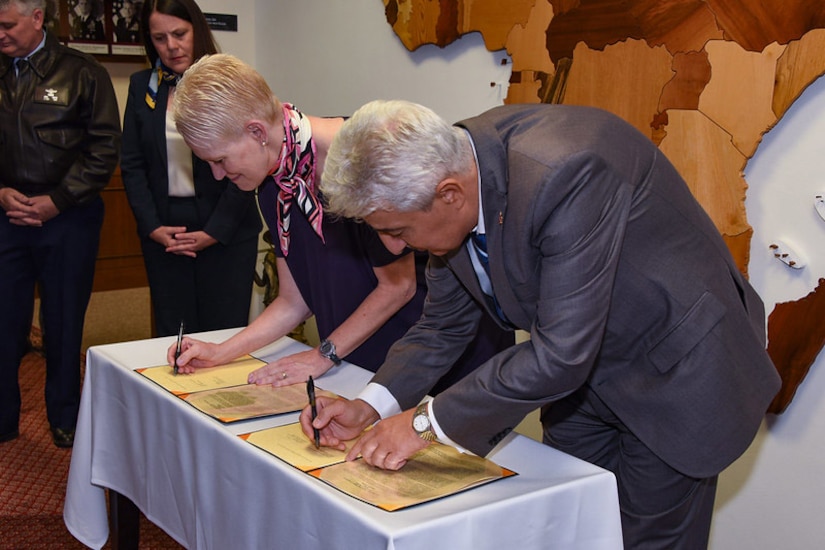 Two people sign paperwork at a table.