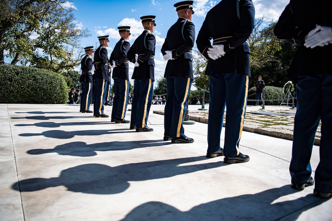 Soldiers stand in a row on pavement that reflects their shadows.