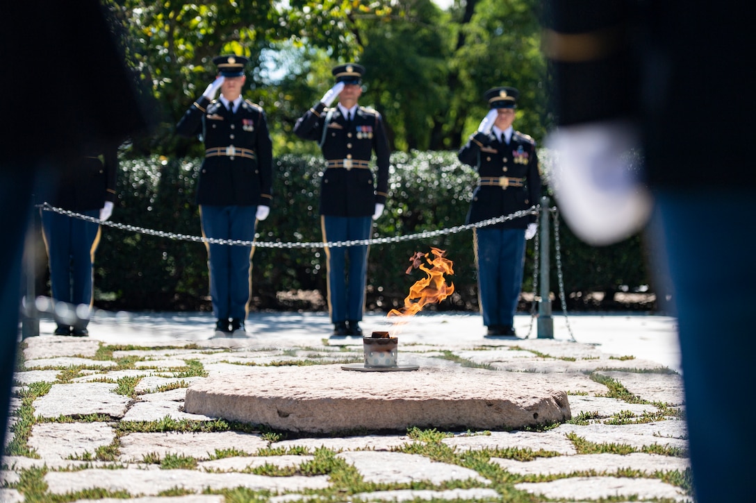 Three soldiers stand at attention and salute at a gravesite.