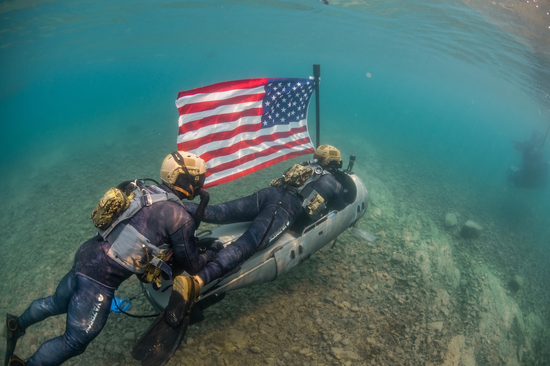 Divers operate a propulsion device with an American flag attached underwater.