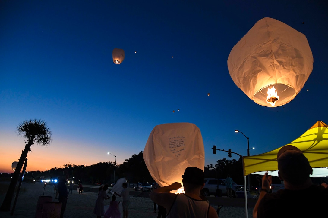 People release paper lanterns into the sky at night.