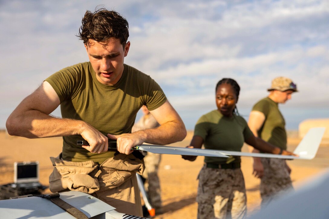 Two Marines hold onto the wing of an unmanned aircraft.
