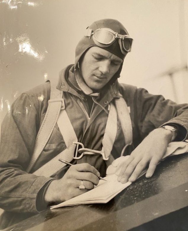 A man wearing goggles and a parachute writes in a book.