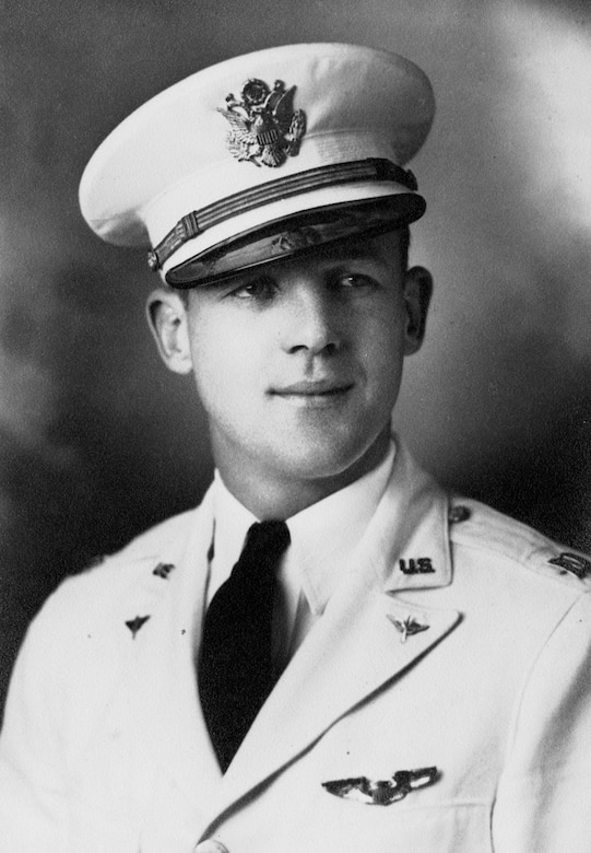A man in a white uniform and cap poses for a photo.