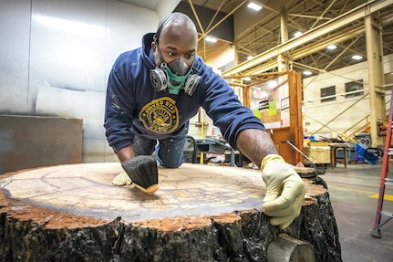 Doriean Sellers, painter, Shop 71, cleans the surface of the newly refurbished Bicentennial Log in the Building 851 Paint Booth before spreading approximately 10 coats of lacquer on it Oct. 6, 2021, at Puget Sound Naval Shipyard & Intermediate Maintenance Facility in Bremerton, Washington. (U.S. Navy photo by Scott Hansen)