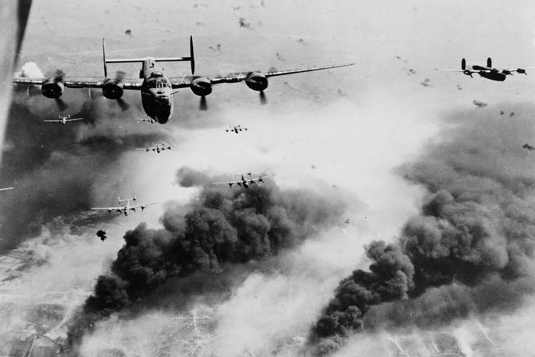 Bomber aircraft fly in the sky above plumes of black smoke.