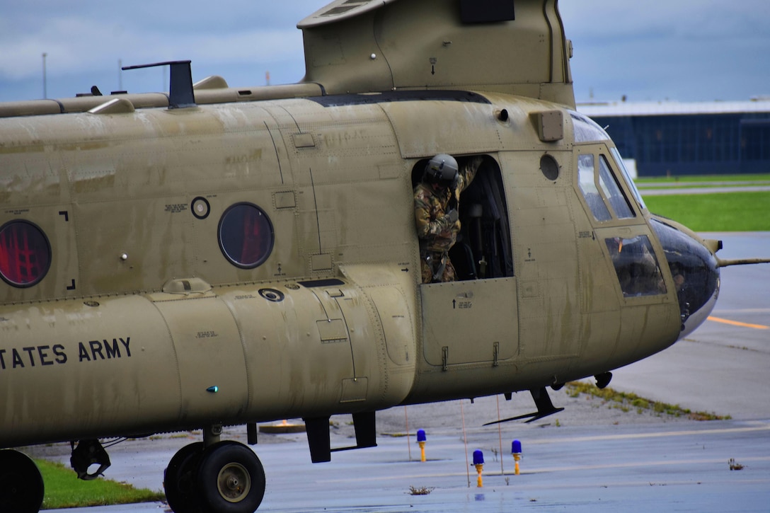 A  service member looks through an opening of an aircraft as it taxis on an airfield.