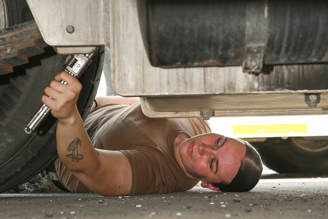 A sailor laying on the ground works on a vehicle.