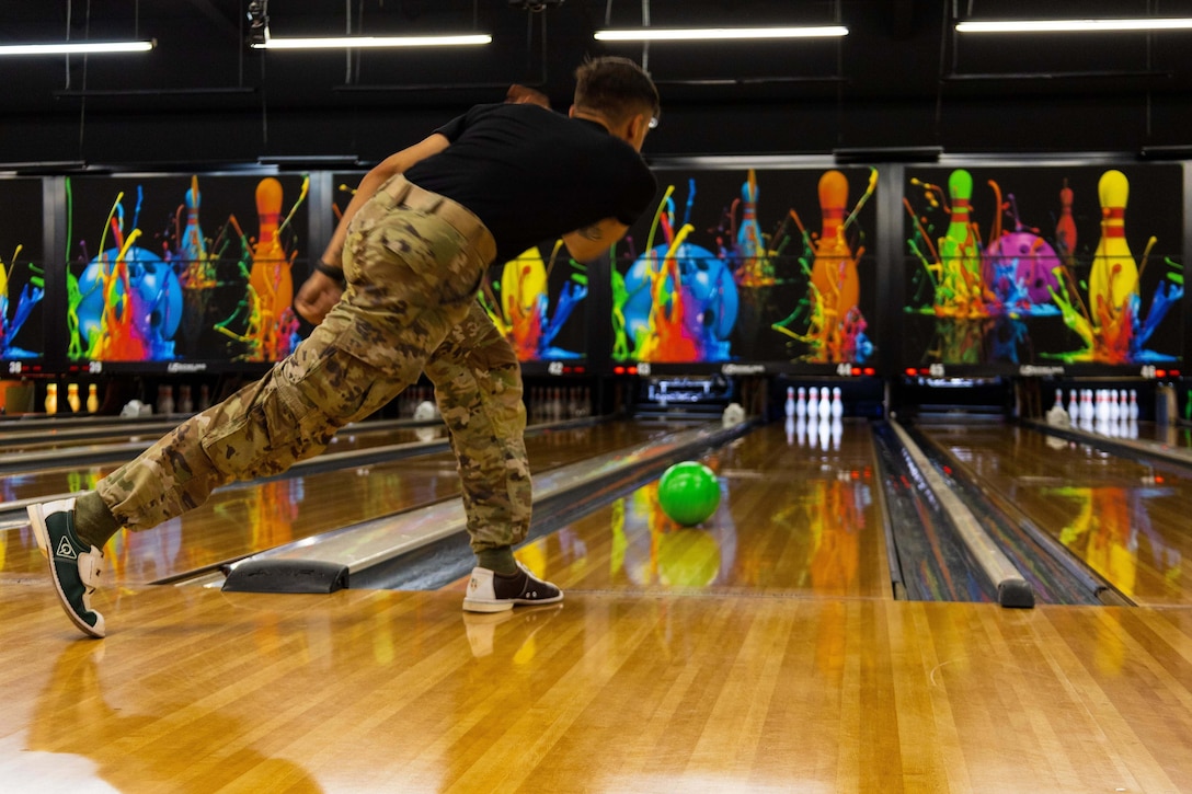 A soldier delivers a bowling ball down the alley.