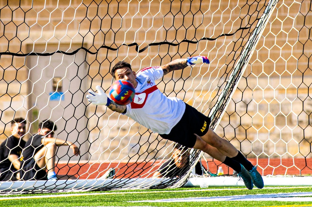 A soldier dives for a soccer ball in front of a soccer goal.