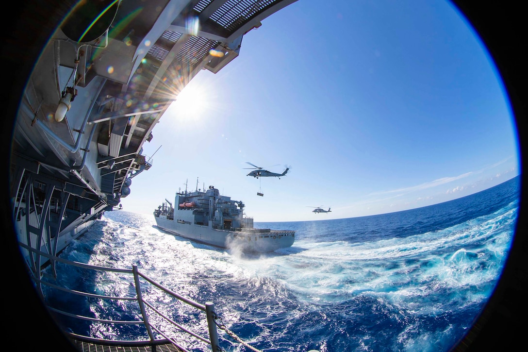 A fisheye view from a ship as two helicopters fly near another ship.