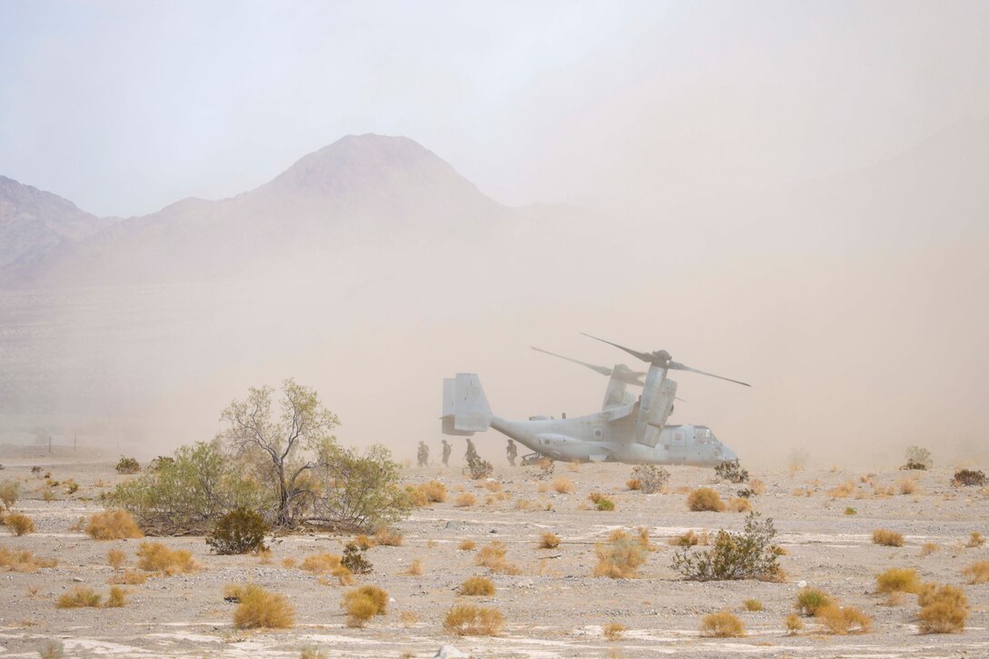Marines exit a parked helicopter in desert area as sand surrounds.