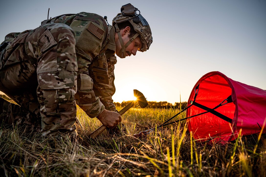 An airman uses a hammer to attach an airfield marker to the ground.