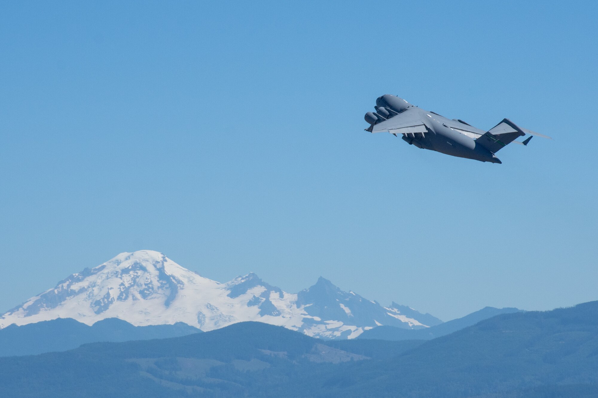 Aircraft ascends over snow-capped mountains.