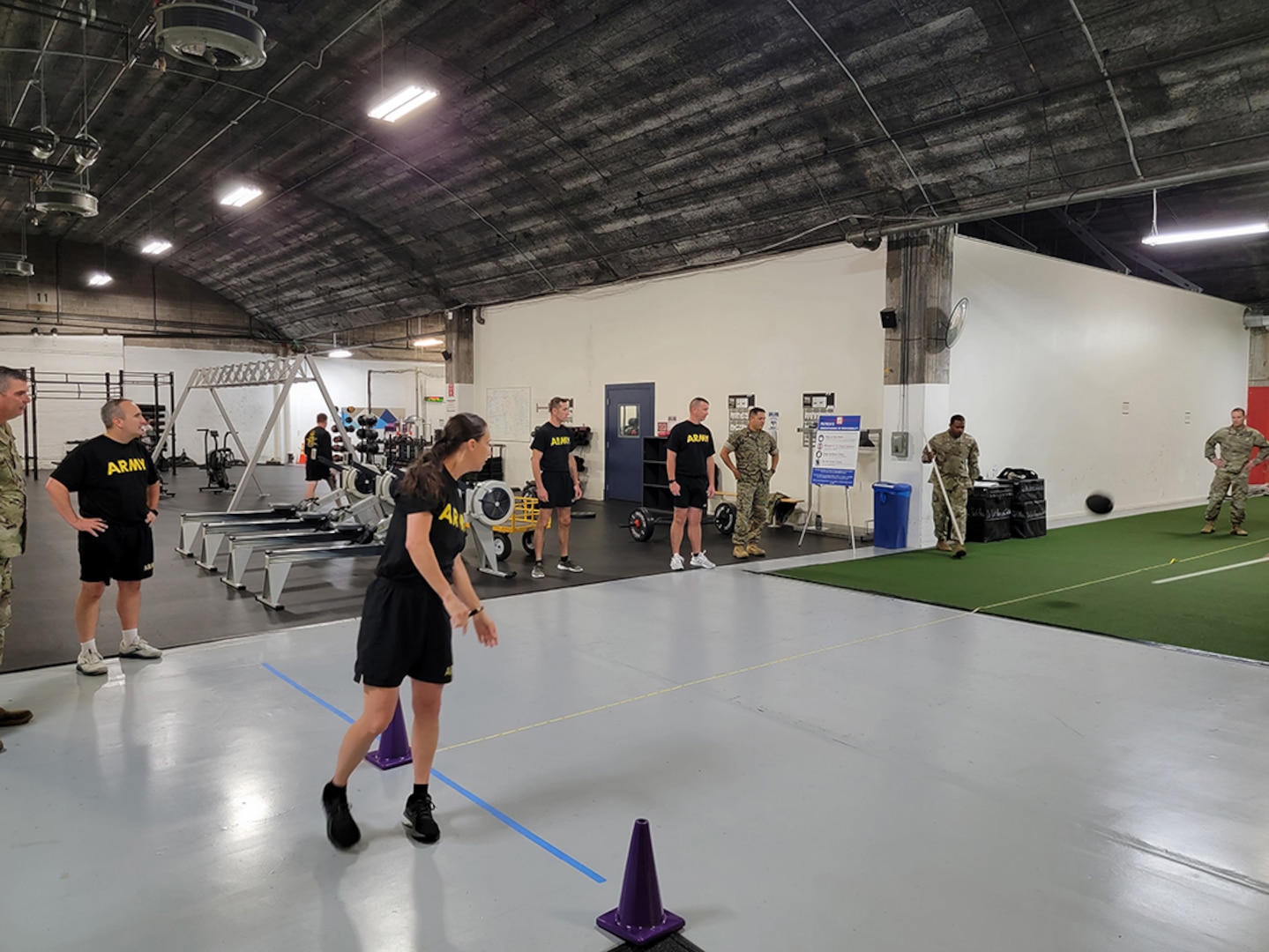 A woman in black fitness gear watches her black ball after she threw it backwards and over her head inside a fitness center.
