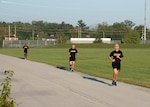 Three men in black Army fitness gear run outside on a track.