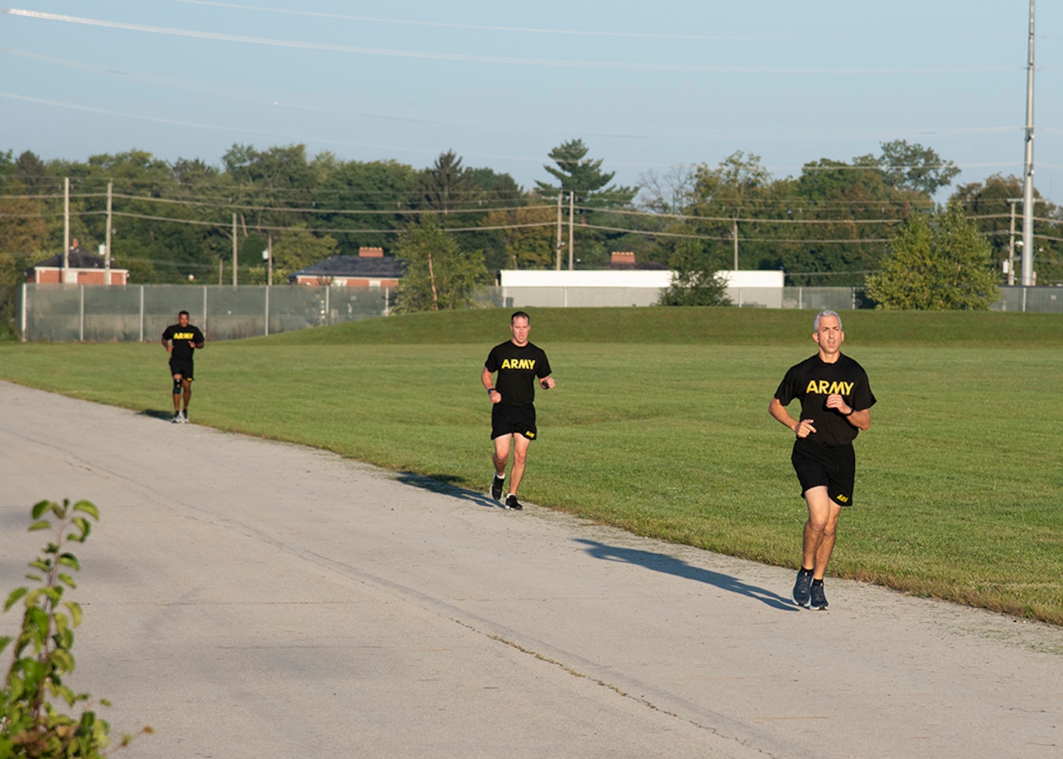 Three men in black Army fitness gear run outside on a track.