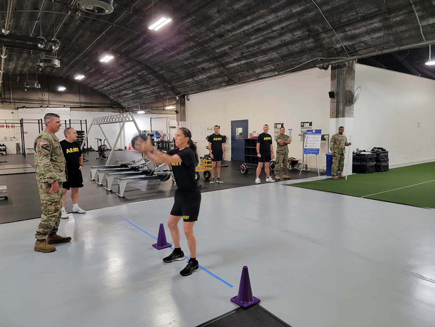 A woman in black fitness gear prepares to throw a black ball over her head.