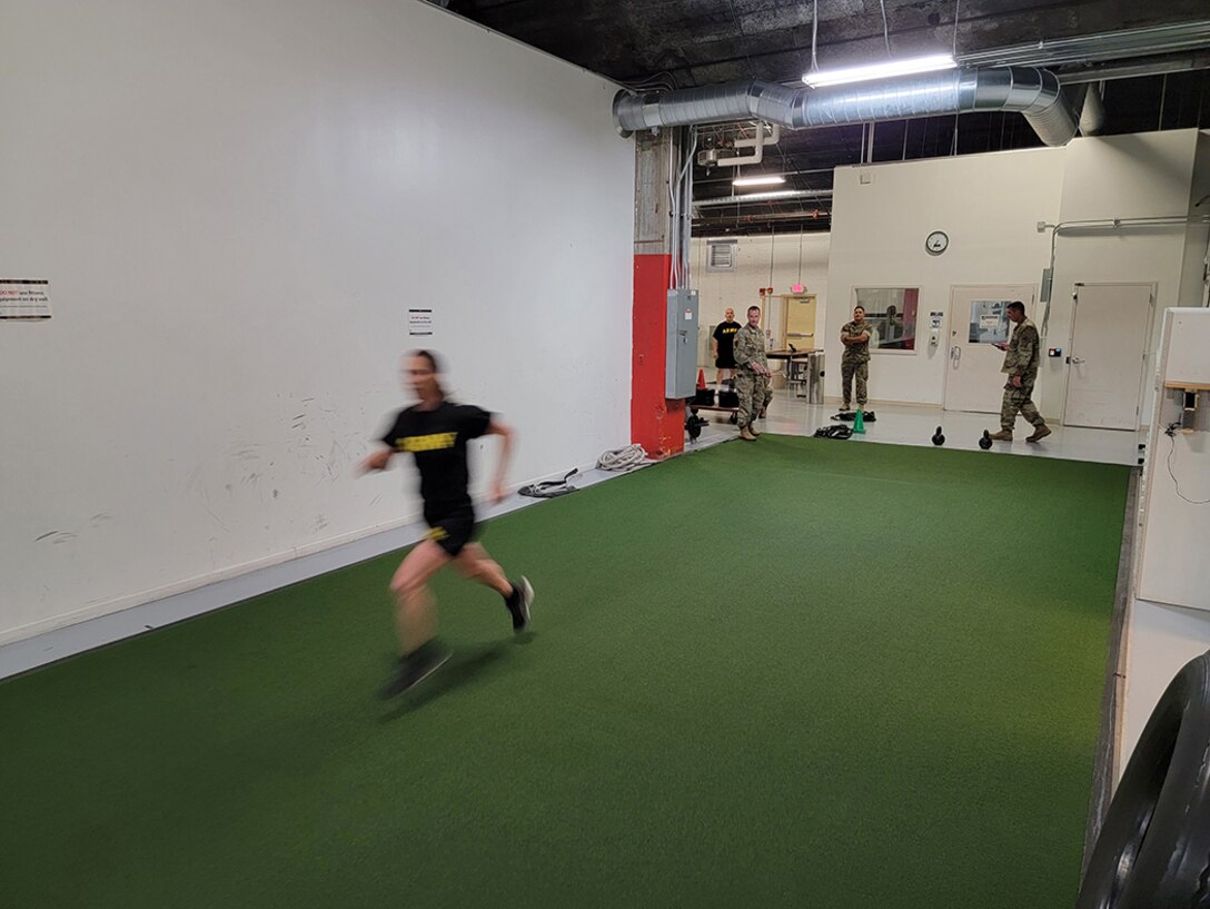 A woman sprints in a open space in a fitness center. She wears black fitness gear.