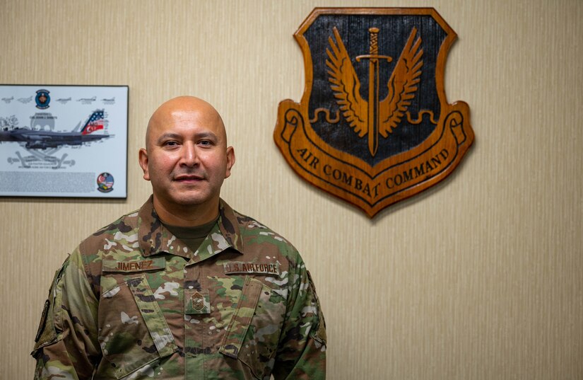Chief Master Sgt. Pedro Jimenez stands in front of ACC Crest.