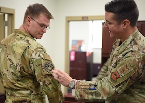 U.S. Air Force Lt. Col. Samuel Logan, 312th Training Squadron commander, places a suicide awareness patch on the uniform of Staff Sgt. Robert Kirkpatrick, 312th TRS instructor at the Louis F. Garland Department of Defense Fire Academy, Goodfellow Air Force Base, Texas, Sept. 8, 2022. Members of the 312th TRS designed the patch, which was lauded for its design and message from several Air and Space Force leaders, who also approved its wear on occupational camouflage uniforms. (U.S. Air Force photo by Senior Airman Ethan Sherwood)