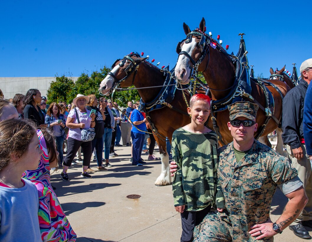 U.S. Marine Corps Gunnery Sgt. Mark A. Daniels, accident investigator with Security Battalion, Marine Corps Base Quantico, poses with his daughter in front of the world-renowned Budweiser Clydesdales at the National Museum of the Marine Corps in Triangle, Virginia, Sept. 23, 2022. The Clydesdales travel to hundreds of appearances each year throughout North America and previously made appearances at the museum in 2010. The event aimed to educate the public about the Marine Corps museum and show appreciation to the local community. (U.S. Marine Corps photo by Lance Cpl. Kayla LeClaire)