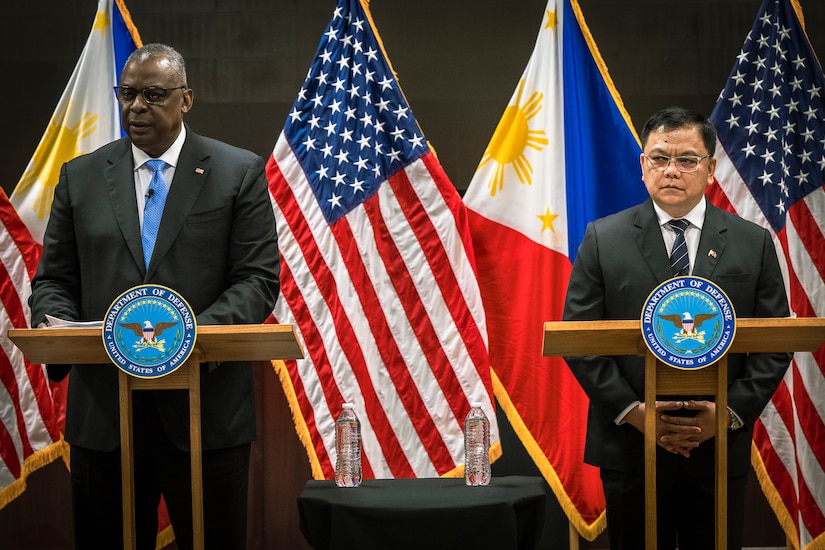 Secretary of Defense Lloyd J. Austin III and another official stand and speak at lecterns in front of U.S. and Philippine flags.