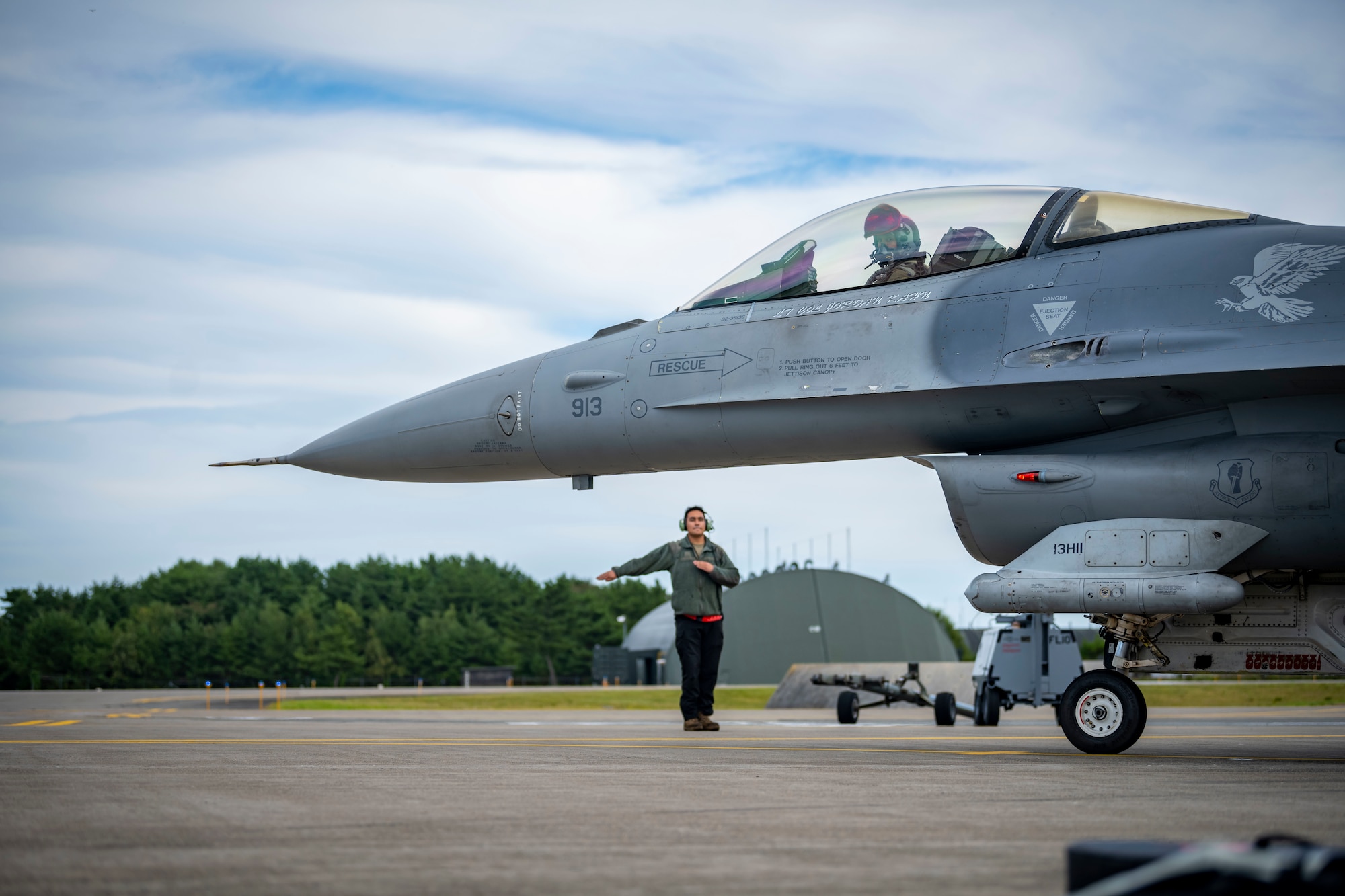 A military member in uniform waves a jet to taxi on the runway