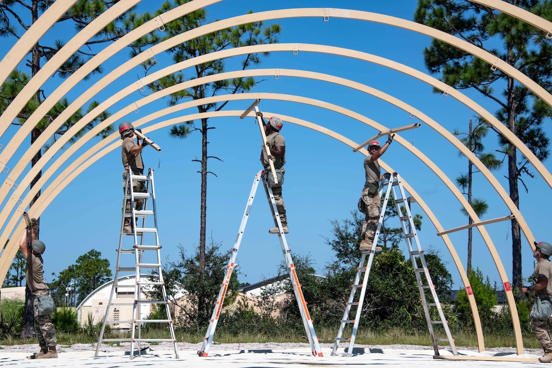 Airmen stand on tall ladders and build a shelter.