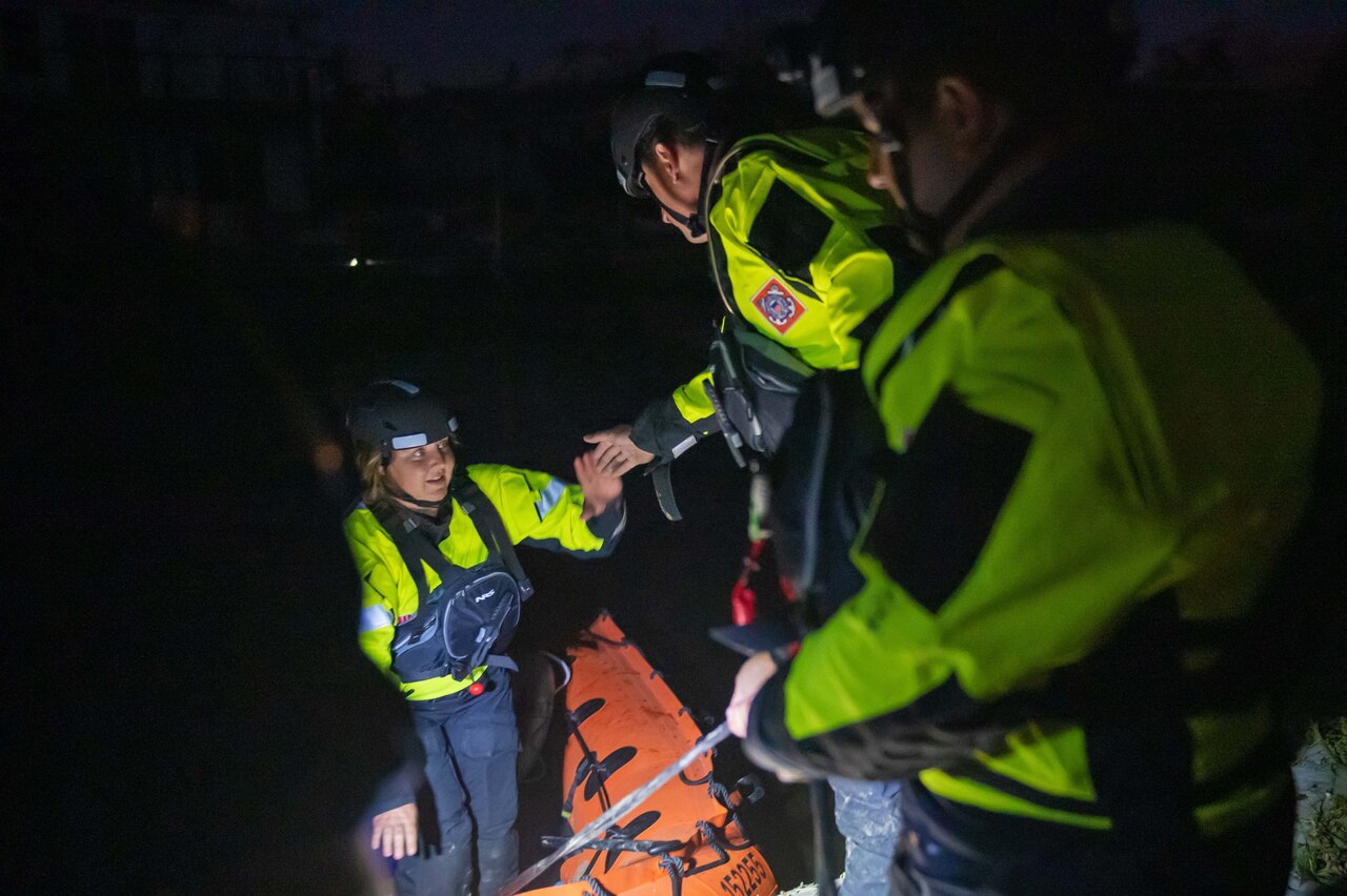 Coast Guard personnel assist a resident onto an inflatable boat at night.