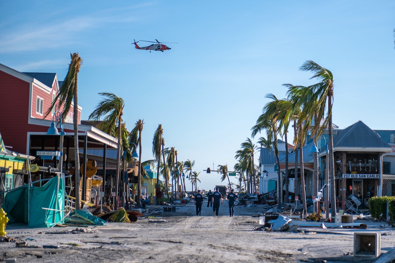 A group of Coast Guardsmen walk down a street devastated by a hurricane.