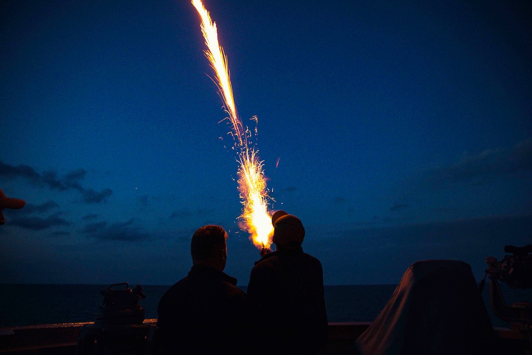 Two sailors fire a flare at night.