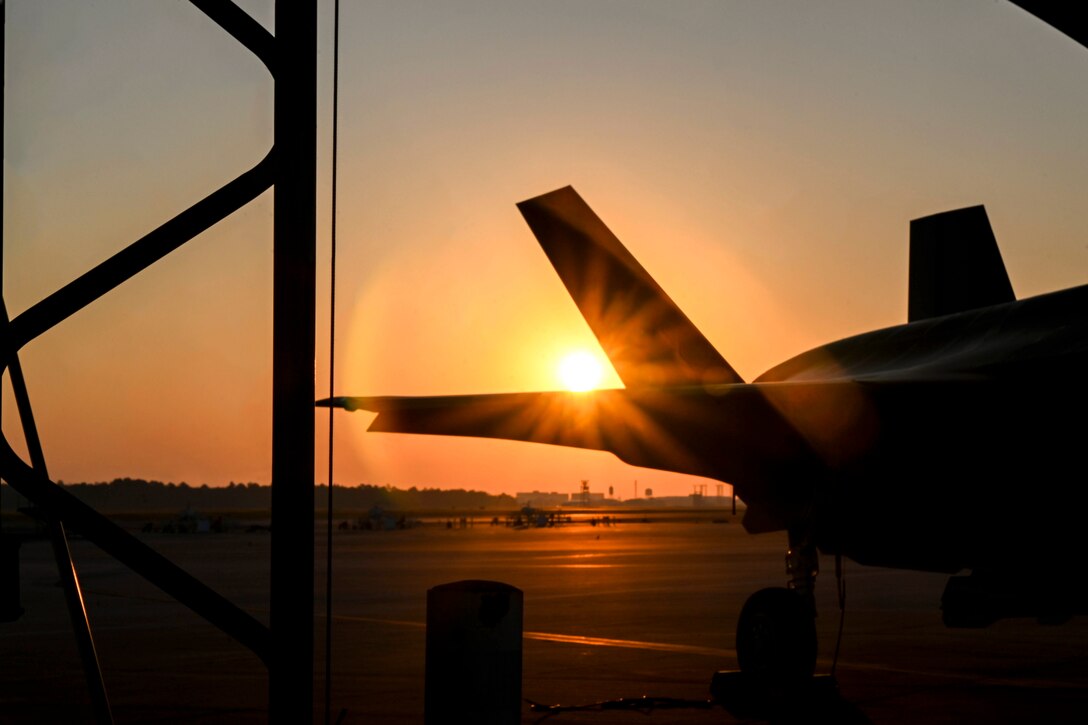 An aircraft sits on a tarmac under a sunlit sky.