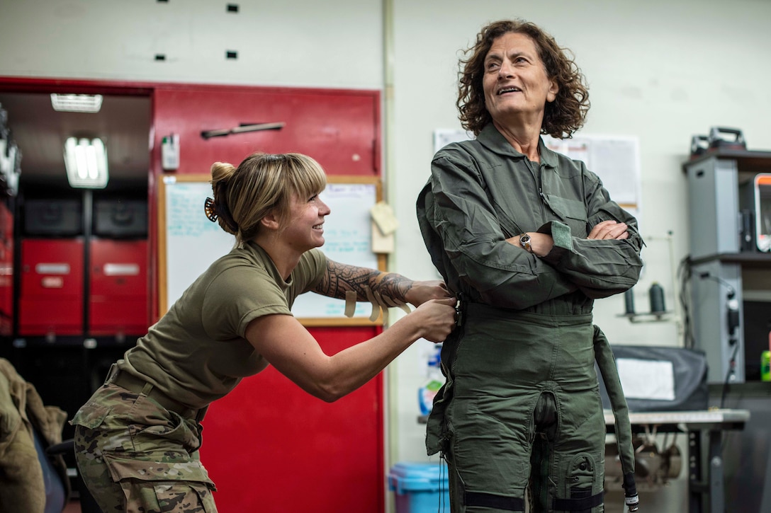 An airman helps a woman fit into a uniform.