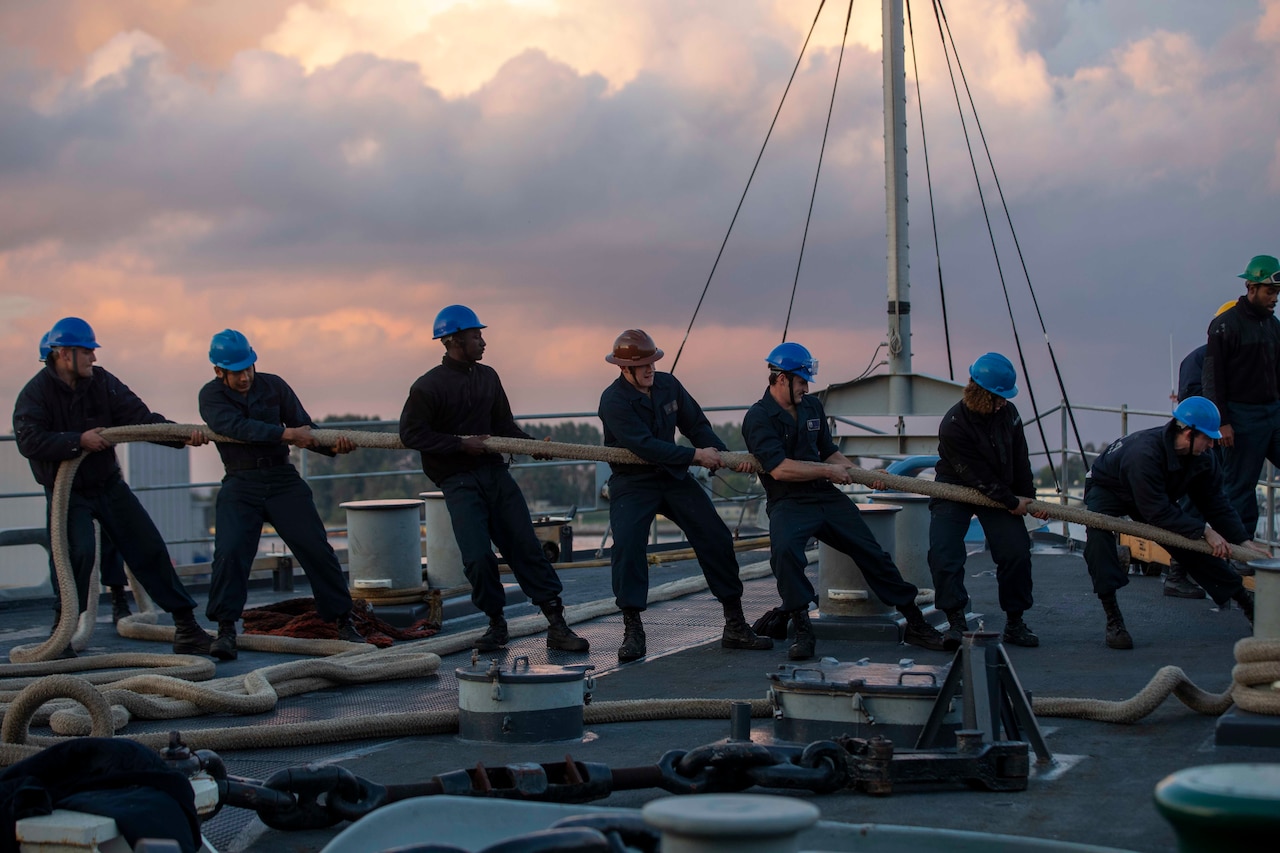 Several sailors, standing in a line, tug on a rope
