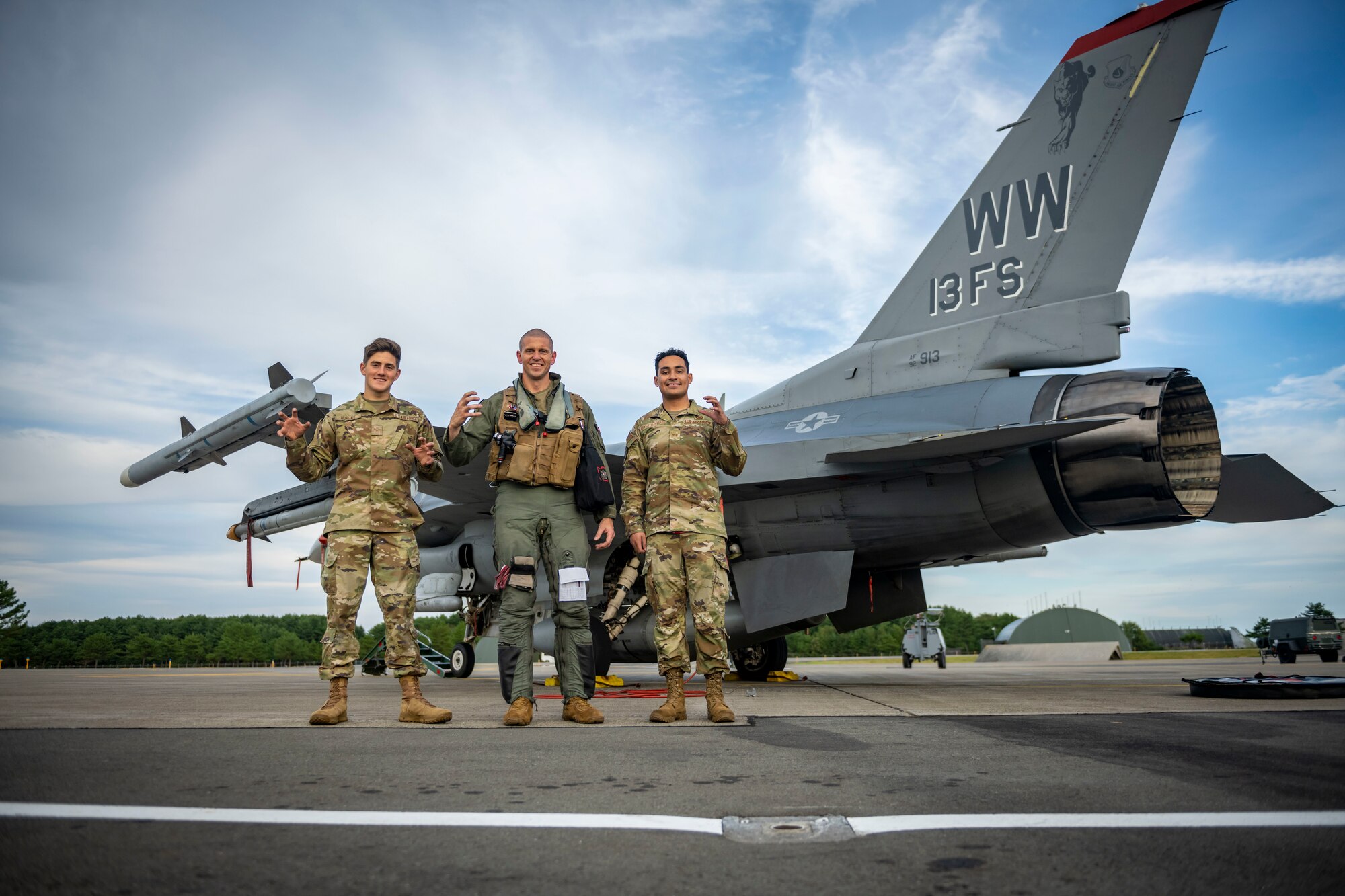 Group of military members in uniform stand in front of a jet and hold up the panther paw hand signal