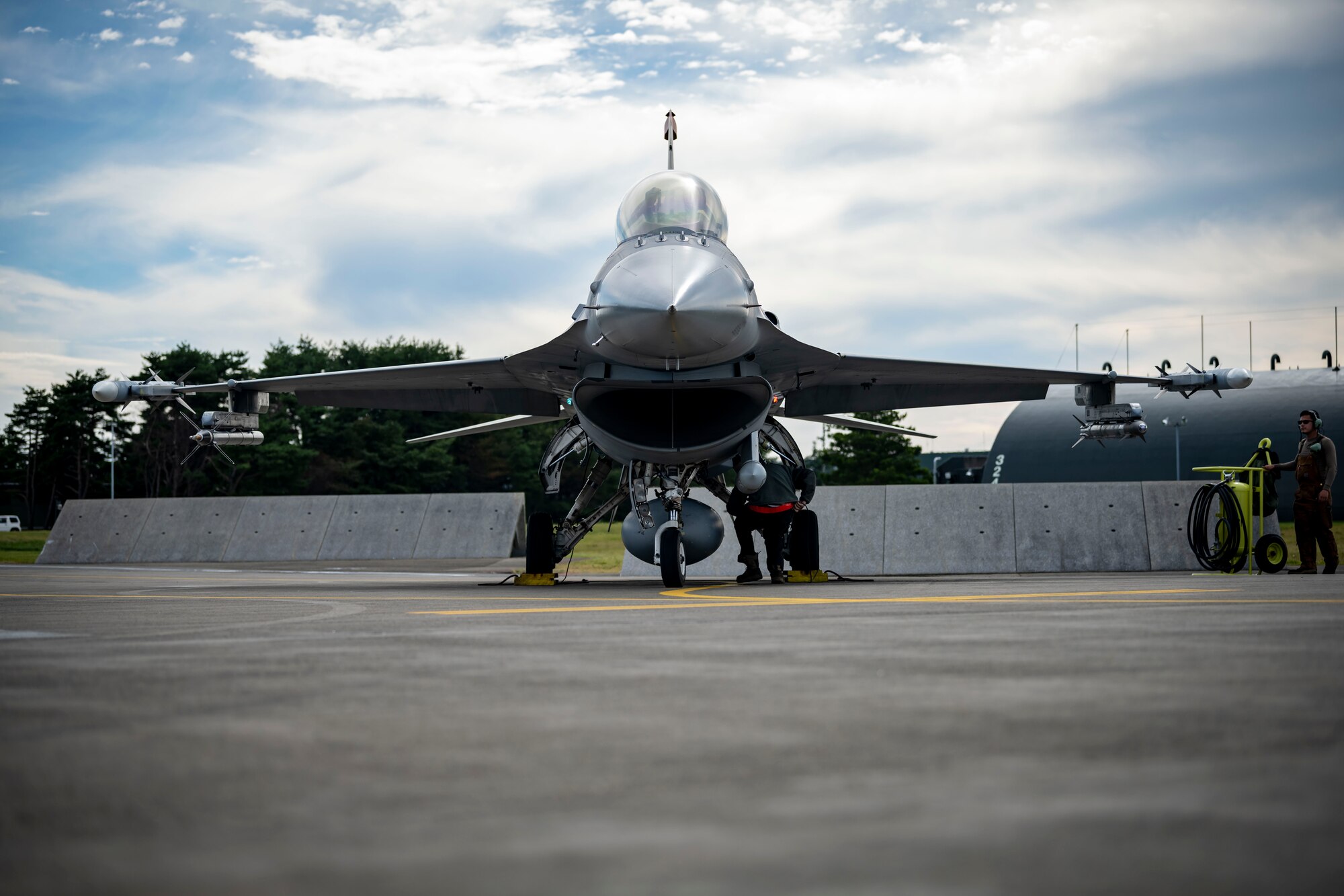 A military member in uniform inspects wheels of a jet.