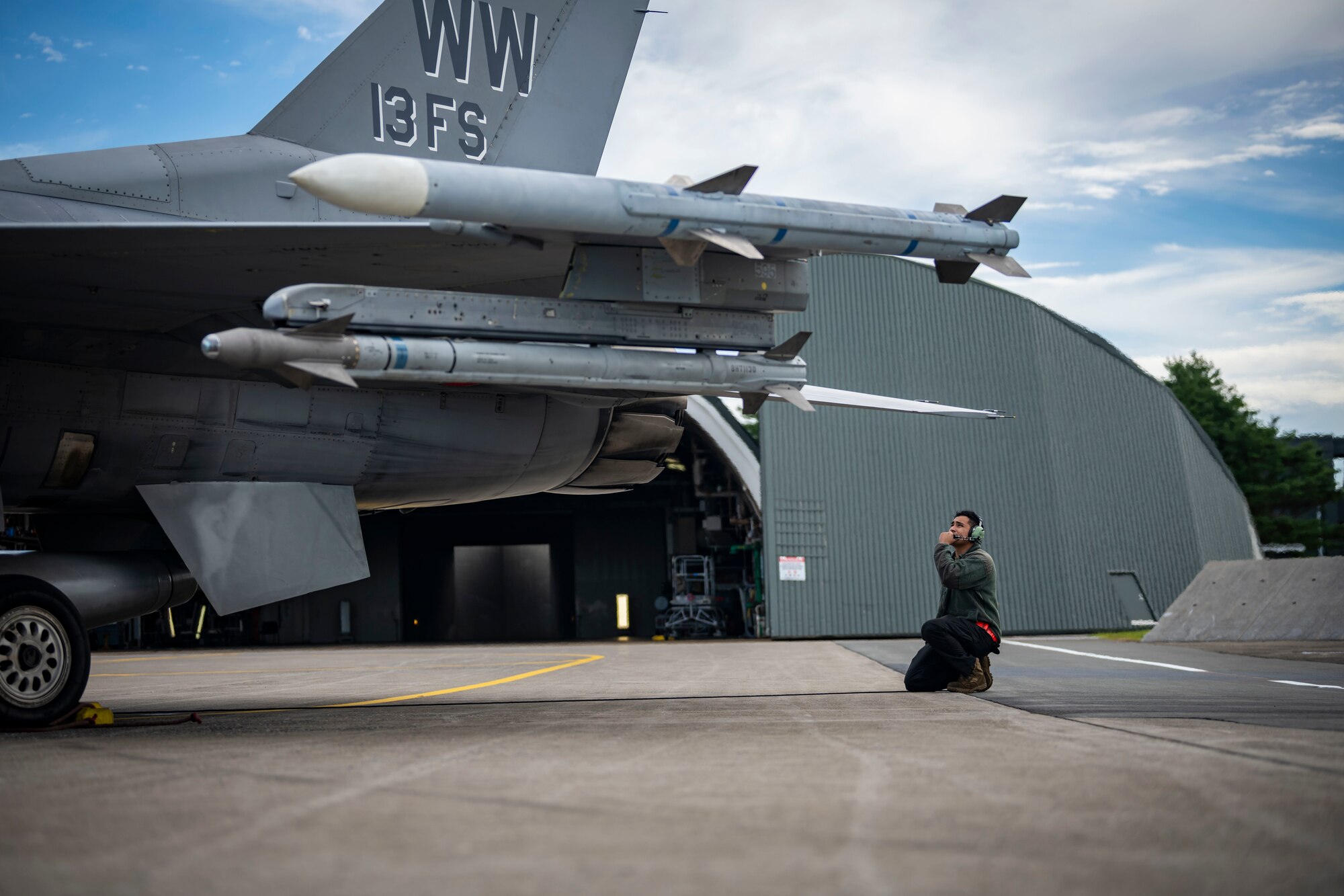 A military member in uniform inspects the engine of a jet.