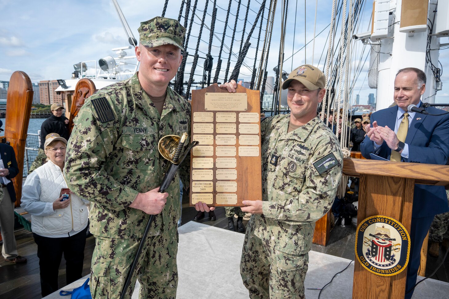 BOSTON (Sept. 30, 2022) Command Senior Chief Seth Miles, right, presents Chief Gas Turbine Systems Technician (Mechanical) Adam Yenny with the 2021 USS Constitution George Sirian Meritorious Leadership Award plaque while underway aboard USS Constitution. The USS Constitution George Sirian Meritorious Leadership Award recognizes a chief petty officer who embodies former USS Constitution crew member George Sirian through their technical expertise, dedication, and leadership. USS Constitution, is the world’s oldest commissioned warship afloat, and played a crucial role in the Barbary Wars and the War of 1812, actively defending sea lanes from 1797 to 1855. During normal operations, the active-duty Sailors stationed aboard USS Constitution provide free tours and offer public visitation to more than 600,000 people a year as they support the ship’s mission of promoting the Navy’s history and maritime heritage and raising awareness of the importance of a sustained naval presence. USS Constitution was undefeated in battle and destroyed or captured 33 opponents. The ship earned the nickname of Old Ironsides during the war of 1812 when British cannonballs were seen bouncing off the ship’s wooden hull. (U.S. Navy Photo Illustration by Mass Communication Specialist 1st Class Grant G. Grady/Released)