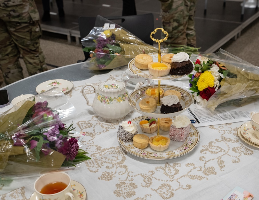 A decorated table has tea, assorted snacks and flowers placed on it