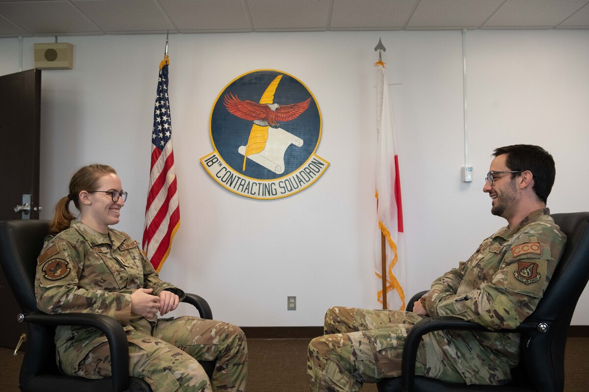 Contracting Airmen sit down and talk in front of their squadron emblem