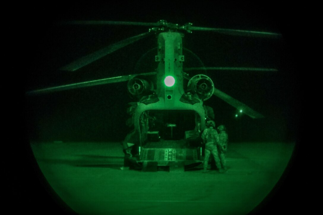 Soldiers stand next to a helicopter at night.