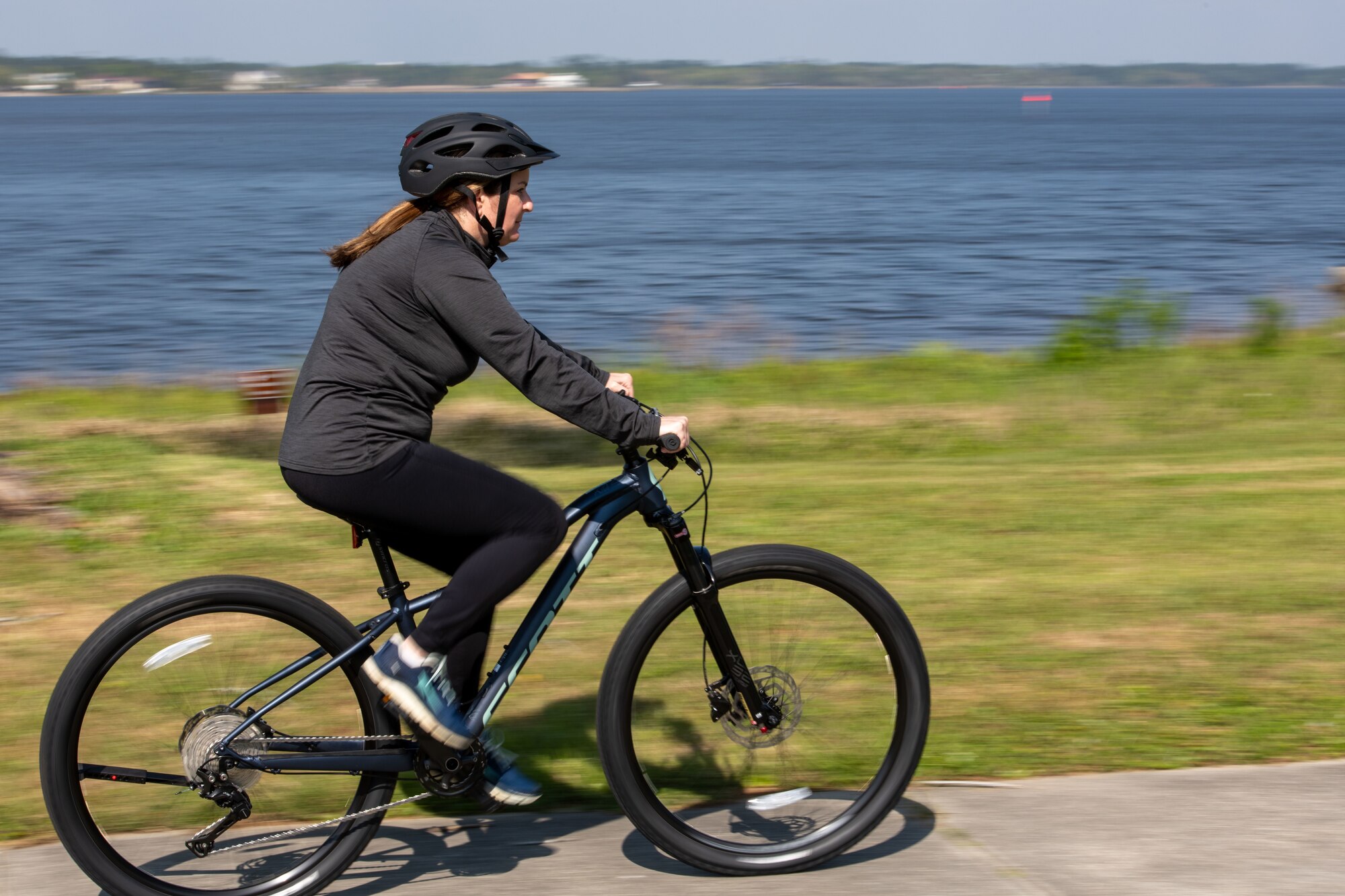 Gilmore rides a bike on a concrete path. Grass and water in the background.