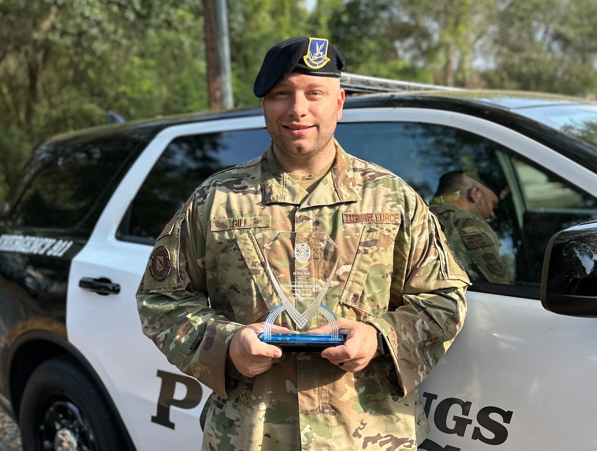 Cody Gill holds an award in front of a police cruiser