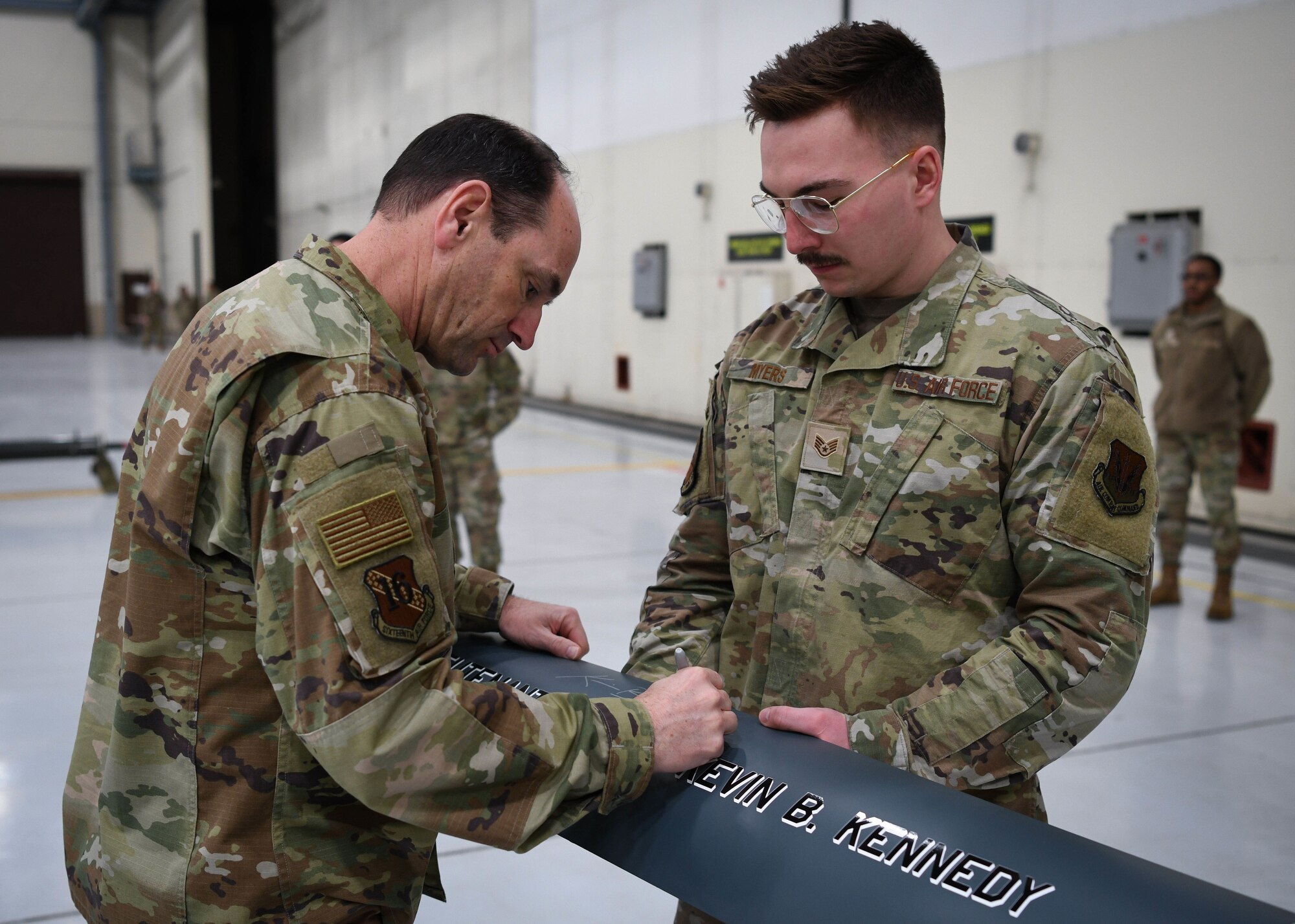 Man in green uniform signs a detached aircraft panel.