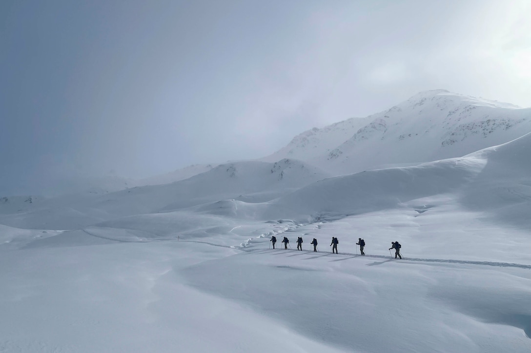 Soldiers walk in a line on a snow-covered mountain.