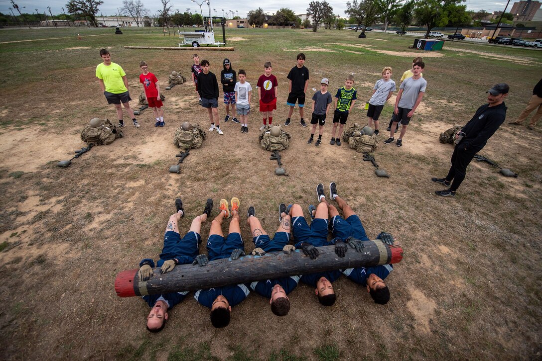 Youth watch as airmen participate in physical training exercises outside.