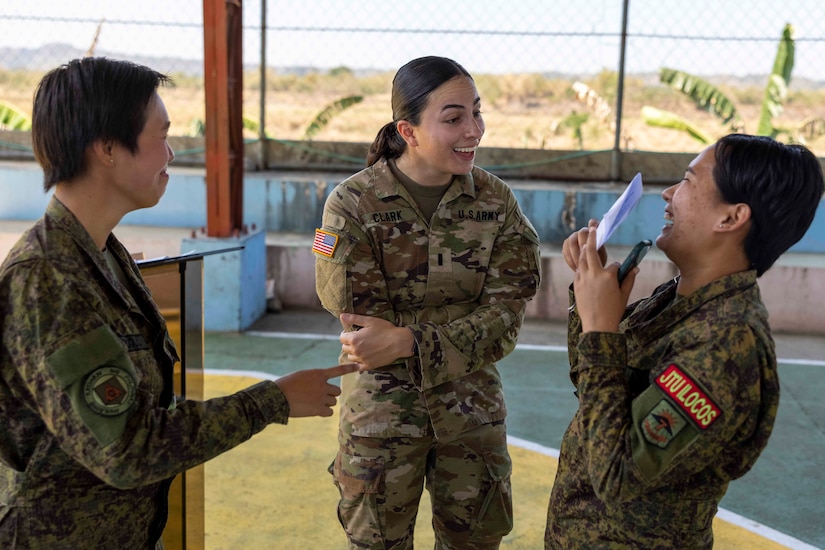Three women in military uniform chat with each other.