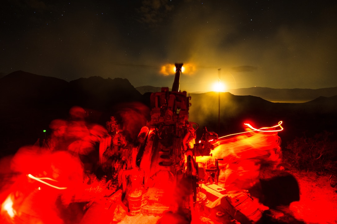 Marines fire a howitzer at night creating a red glow.