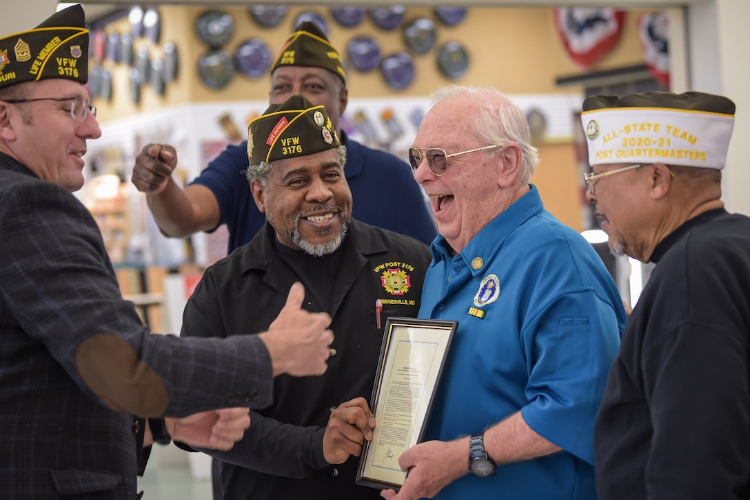 A group of men stand together and laugh, one holds a plaque.